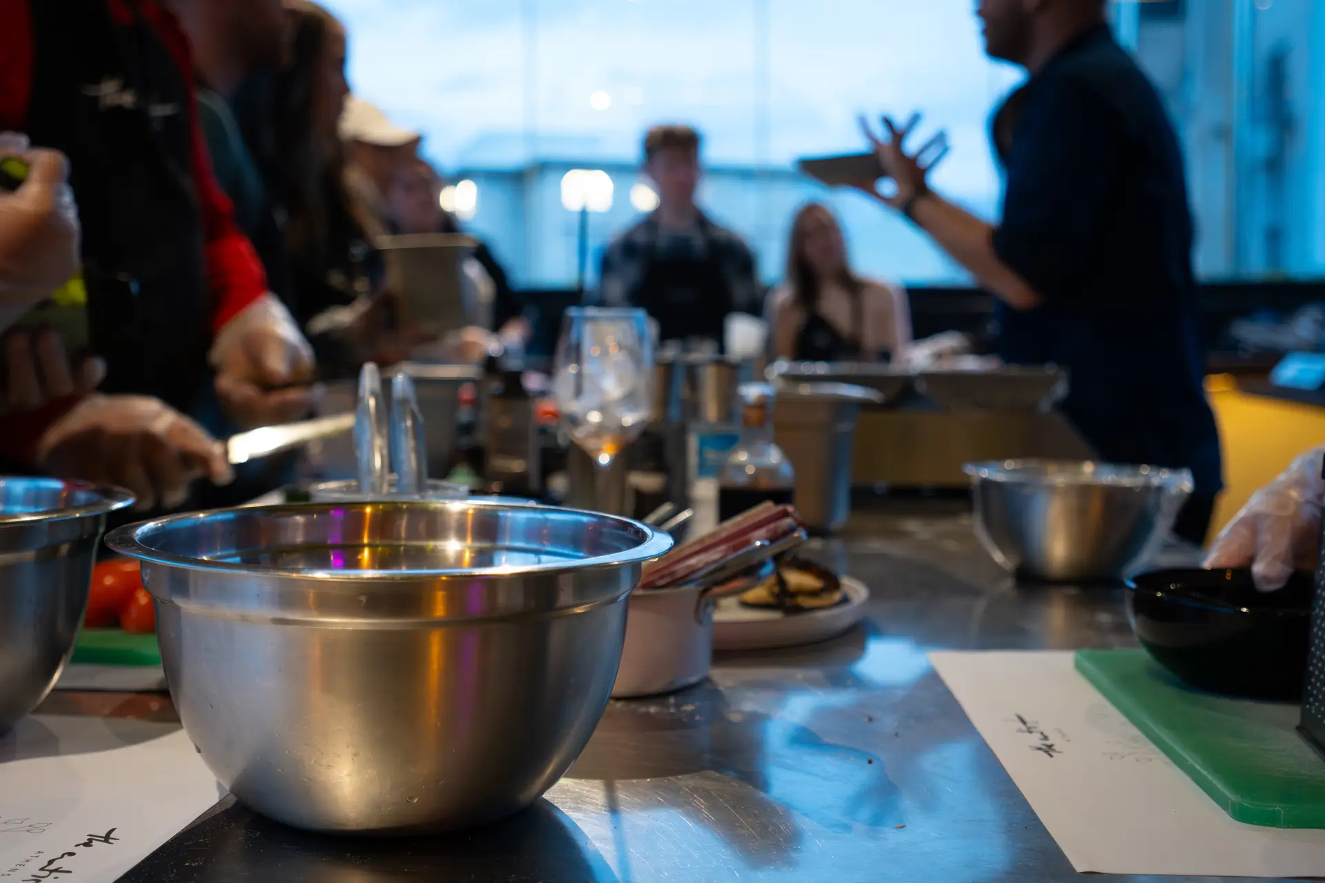 Cooking class in full swing — steel bowl in foreground, chef gesturing in background